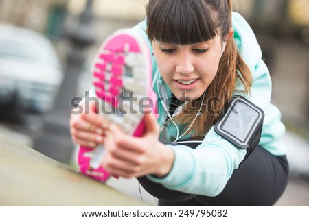 Young Woman Doing Stretching Exercises before Jogging. Focus on the Face. Town Setting in the background.