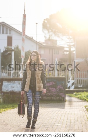 Young Woman Walking at Park in the Morning. The Girl is Looking Ahead. The Park is in a Residential Area, there are some Houses on Background.