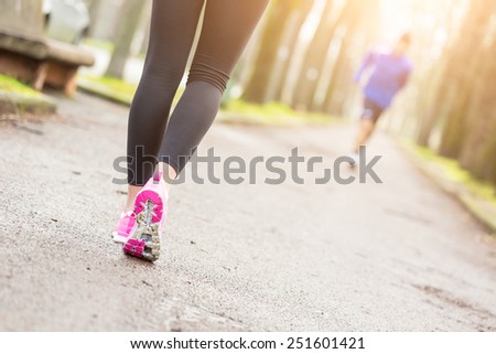 Female Runner Shoes closeup before Running at Park. Shallow depth of Field, focus on rear shoe. On background the Foothpath and some Trees.