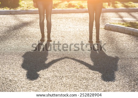 Shadows of Female Twins Holding Hands in the City. The Shadow is the Main Subject of the Photo. Girls are standing and Holding Hands. Backlight Shot. Focus on Shadow.