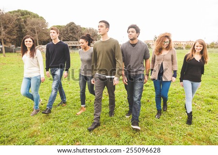 Multiethnic group of friends at park walking and enjoying time all together. Mixed race group with caucasian, black and asian people. Friendship, lifestyle, immigration concepts.