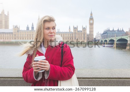 Beautiful blonde young woman holding cup of tea in London with Westminster palace and Big Ben on background.
