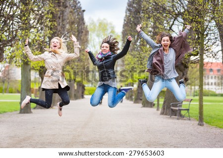 Group of women jumping at park in Copenhagen. They are in their twenties and they are wearing smart casual clothes. Happiness, friendship and success concepts.