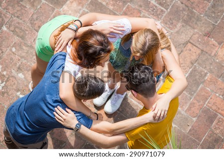 Group of teenagers embraced in circle, aerial view. They are two girls and two boys, looking each other