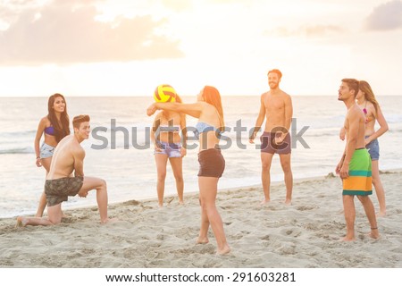 Multiracial group of friends playing with ball on the beach. There are four girls and three boys, with a filipina girl and a spanish boy.