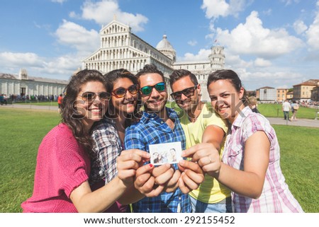 Group of tourists or friends showing the selfie they took in Pisa, Italy, with famous leaning tower on background. They are two men and three women. Lifestyle, friendship and travel concepts.