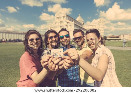 Group of tourists or friends showing the selfie they took in Pisa, with famous leaning tower on background. They are two men and three women. Friendship and travel concepts. Vintage filter added.