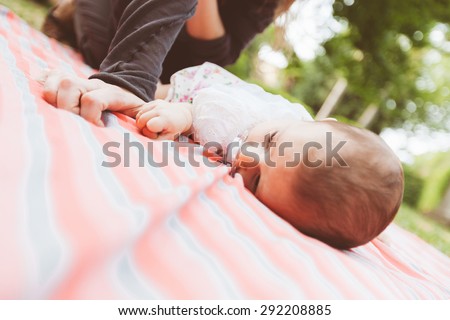 Baby daughter lying down and hugging tightly mothers finger. They are at park, the mother is smiling and cuddling her daughter. Vintage filter added.