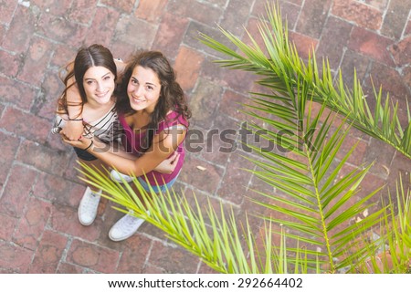 Portrait of two beautiful girls taken from above. They are embraced and looking up at camera. Lifestyle and friendship concepts.