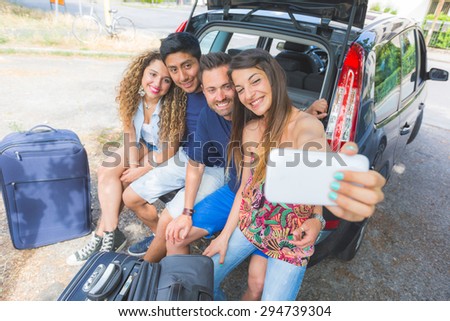 Group of friends taking a selfie in the back of the car before leaving for vacations. They are a mixed race group of four persons, two caucasian and two hispanic.