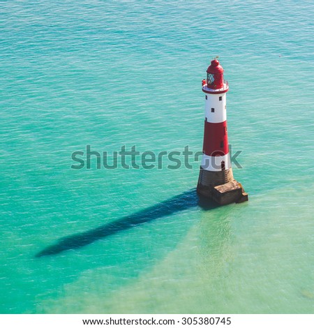 Lightouse and sea in southern England next to Eastbourne. Photo taken from above, the lighthouse is red and white, with its shadow on water surface.