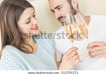 Happy couple making a toast on the bed. It could be on Valentine\'s day or for birthday, they\'re looking each other and smiling. Setting could be luxury home or hotel bedroom.
