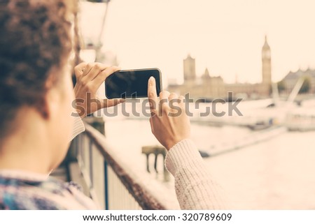 Young woman taking photo of Big Ben in London with her smart phone. She is a mixed race woman on her late twenties, with light dark skin and curly hair. Tourism and lifestyle concepts