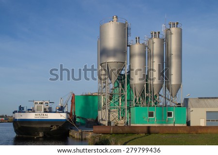 Burgum, Sumar, the Netherlands, april 27, 2015. Noppert Concrete Factory. A concrete production site. the silo\'s are shining nice in the sunset. Next to the site is a ship waiting for cargo.