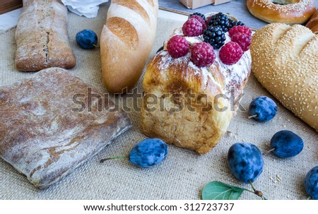 Assortment of fresh breads, pastries, ciabatta, cake with powdered sugar, berries, plum and raspberry on the table