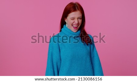 Smiling playful happy redhead teen girl in blue sweater blinking eye, looking at camera with toothy smile, winking and flirting, expressing optimism. Young pretty adult woman on pink studio background Foto stock © 