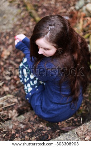 Back of a young woman with long brown wavy hair sitting on a step waiting