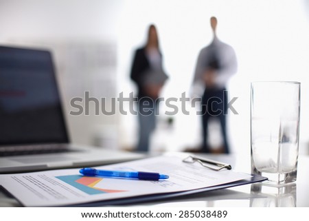 Laptop  computer with folder on the desk ,two  businesspeople standing in the background.