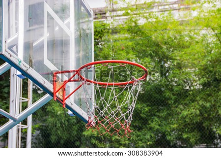 Basketball hoop in the park with green trees as background.