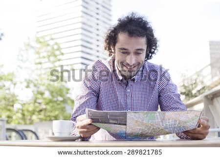 Handsome smiling man consulting a guide in a restaurant terrace. Vacation concept.