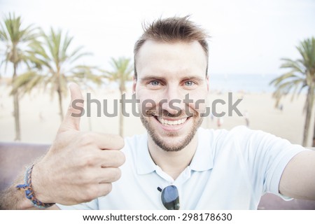 Man taking self portrait and showing thump up. Smiling. Vacation selfie.