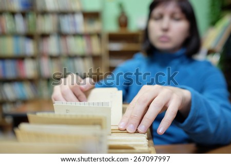 Librarian woman searches something in card catalog