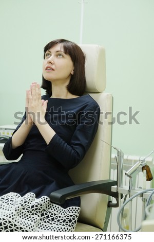 Woman sitting in the chair, folded his hands to pray and looking up. At the reception of an ENT doctor