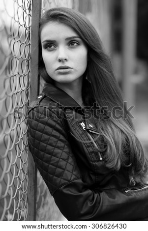 Fashionable black and white photo from a magazine. beautiful young rocker in a heavy leather jacket, with long beautiful black hair posing on the background grid and Park