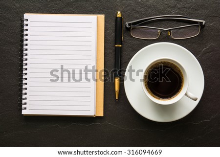 Coffee and a notebook and pen and glasses on a black background.