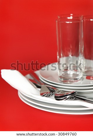 Pile of white plates, glasses with forks and spoons on silk napkin. Focus accent on front.  Red background