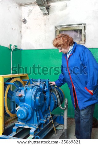 Operator woman-engineer  in machine room (elevator) check the mechanical equipment.