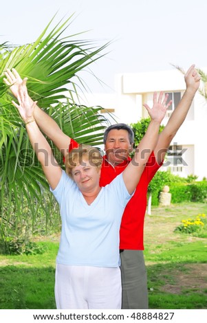 Elderly couple near the palm-tree with hands-up.