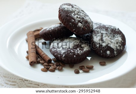 Chocolate muffins on a white plate decorated with cinnamon sticks, coffee beans and sugar powder, close up