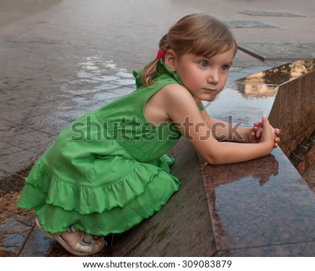 An urban close up serious portrait of a little girl near the granitic parapet wall of a fountain