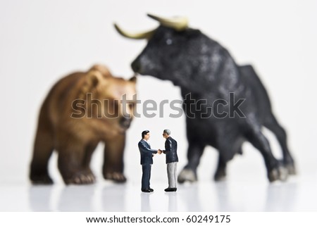 Business figurines shaking hands placed in front of bull and bear figurines.