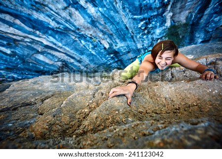 female rock climber climbs on a rocky wall, Keep a hand on the rock and laughs. focus on the hand
