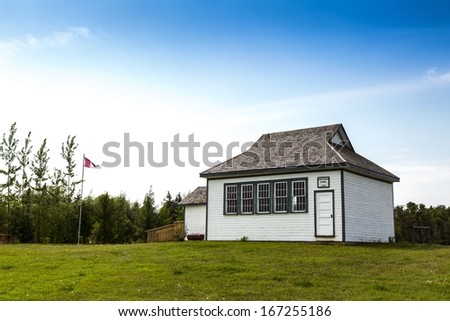 An old vintage school house with a Canadian flag in the yard