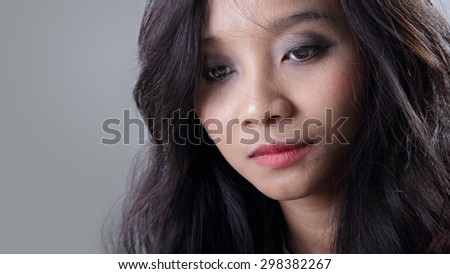 Close up face of young Asian woman looking down with melancholic expression, on grey background