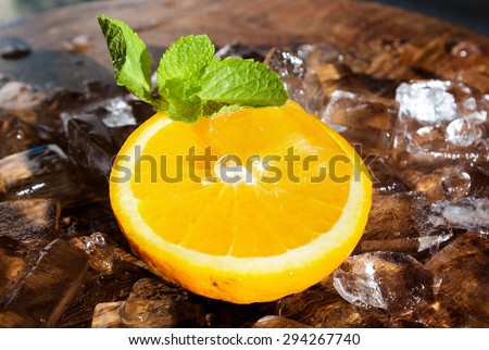 A slice of orange with a mint leaf is lying onto layer of ice cubes in a hot sunny day. Summer fruity cocktails are great way to deal with the heat and high air temperature.