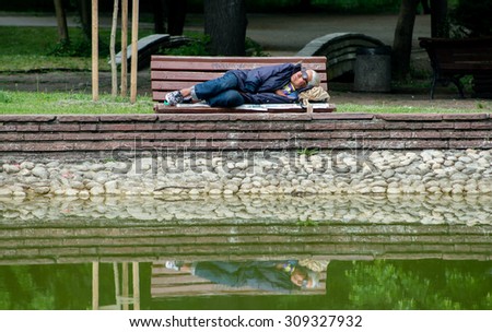 A homeless man is sleeping on a bench next to a pond in the city park, May 05, 2015, Sofia, Bulgaria. Homeless people use the night for searching food, while spending the daylight sleeping.