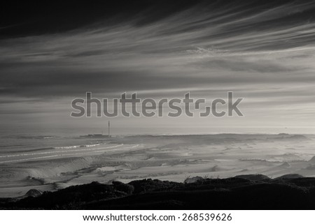 Dramatic clouds over seascape with sand dunes and man-made structure in the distance