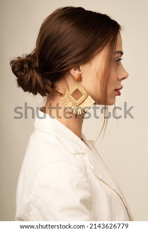 Medium close-up shot of a woman with boho rhombus earrings with a fringe. These earrings are decorated with raffia weaving. The woman in a white shirt with earrings is posing on a beige background. Stockfoto © 