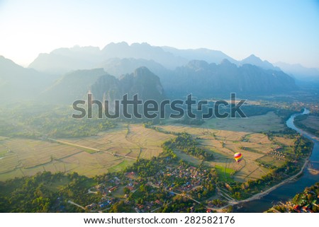 Striped hot air balloon flying over earth, evening landscape and the city with little houses, a river in Laos to Vang Vieng.Laos.