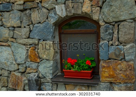 The monastery of stone, an old Church in the mountains. Alan Svyato-Uspensky monastery, which is located in Fiagdon.Hidixys.A window on stone wall background.Red flowers in a pot.