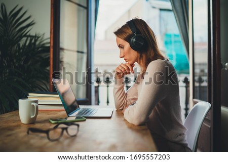 Concentrated student girl learning online having video call via laptop computer sitting at home interior near open balcony, female entrepreneur working remotely from home office using modern computer