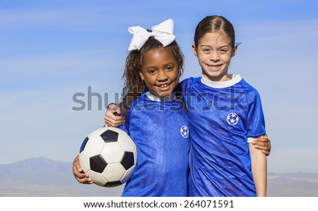Cute, young african american and hispanic female soccer players holding a ball with a simple blue sky background