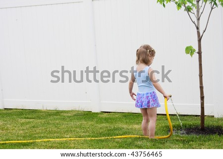 A young girl waters a young tree in her back yard helping it grow