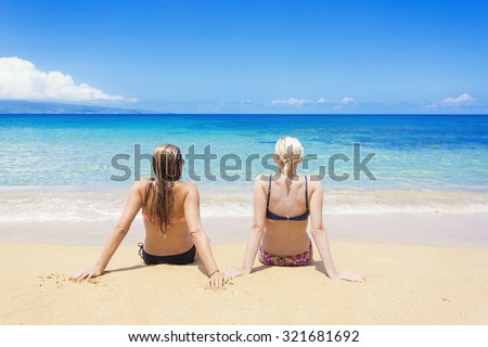 Two women sun tanning on a sunny beautiful beach. View from behind of women relaxing while on a beautiful island vacation
