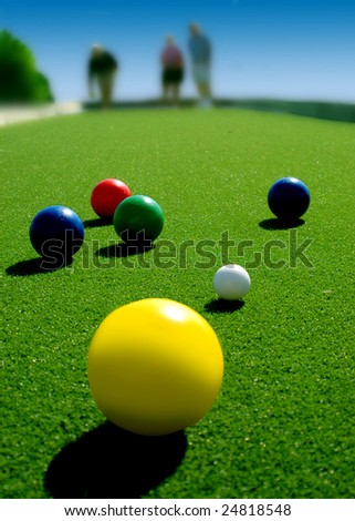 Bright colored Bocce balls on brilliant green court. Three players in background.