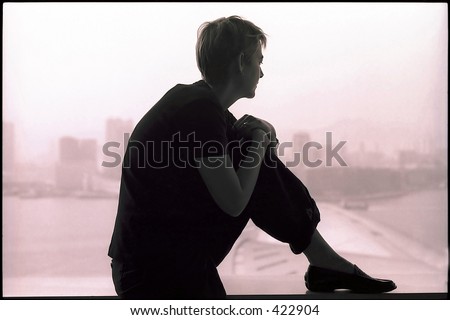 Silhouette of a pensive woman sitting on the window ledge of a room overlooking Hong Kong harbour